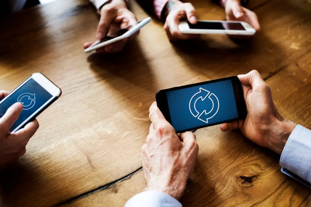 Image of Business people sitting at a table using smart phones with sync icon for a catalog sync