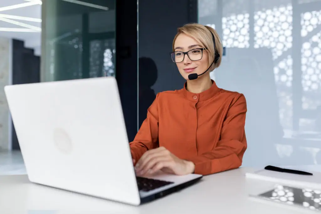 Successful support team member with video call headset working inside modern office online customer support worker using laptop typing on keyboard successful white glove support