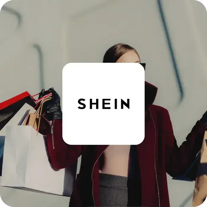 SHEIN logo on a white card over a woman carrying shopping bags in a burgundy coat