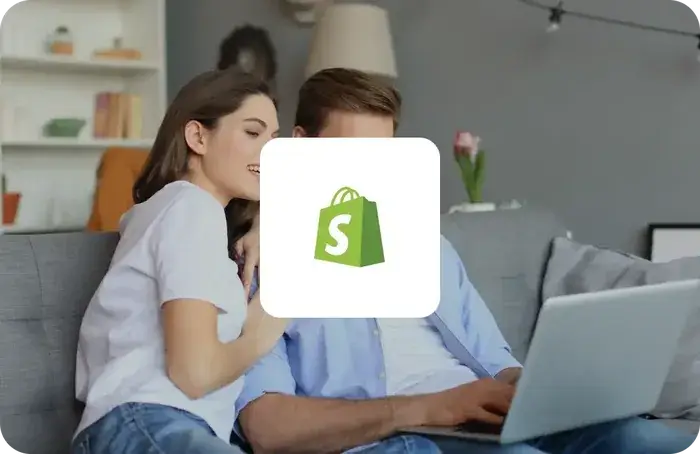 Shopify logo on a white card over a couple browsing a laptop together on a sofa