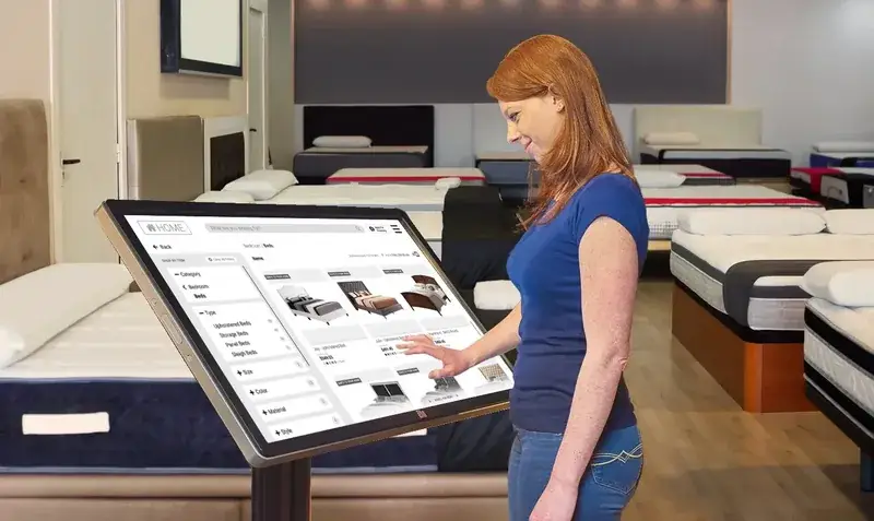 Woman with red hair browsing bed frames on a floor stand kiosk running Enterprise Kiosk Software in a mattress showroom Woman with red hair browsing bed frames on a floor stand kiosk running Enterprise Kiosk Software in a mattress showroom