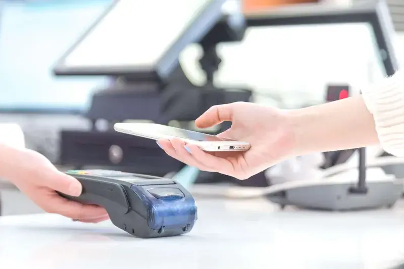 Customer tapping a smartphone on a contactless payment terminal at a retail counter Customer tapping a smartphone on a contactless payment terminal at a retail counter